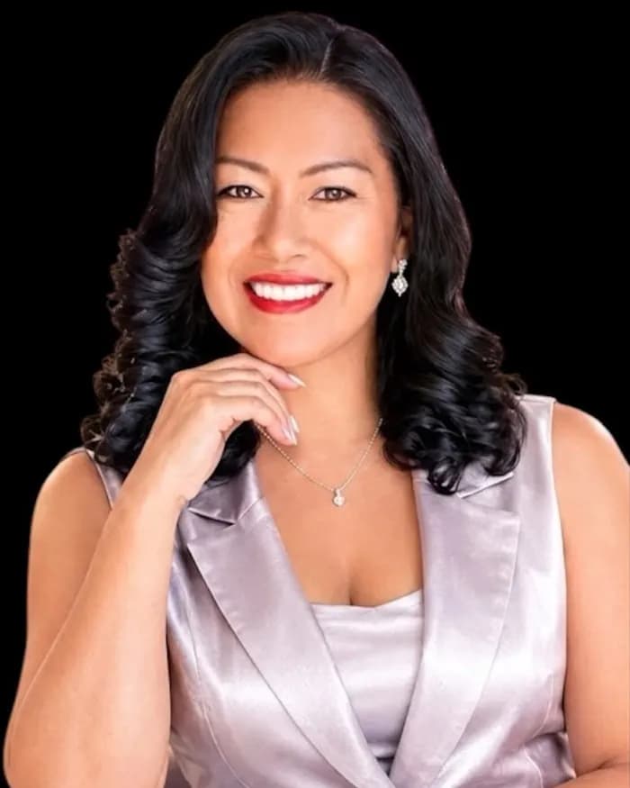 Lucy Peña sentada, con traje plateado, sobre fondo negro