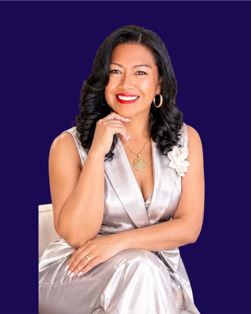 Lucy Peña sentada, con traje plateado, sobre fondo azul índigo