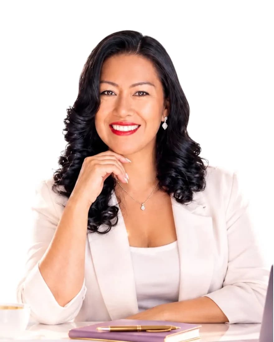 Lucy Peña sentada a su escritorio, con blazer color crema y una libreta lila